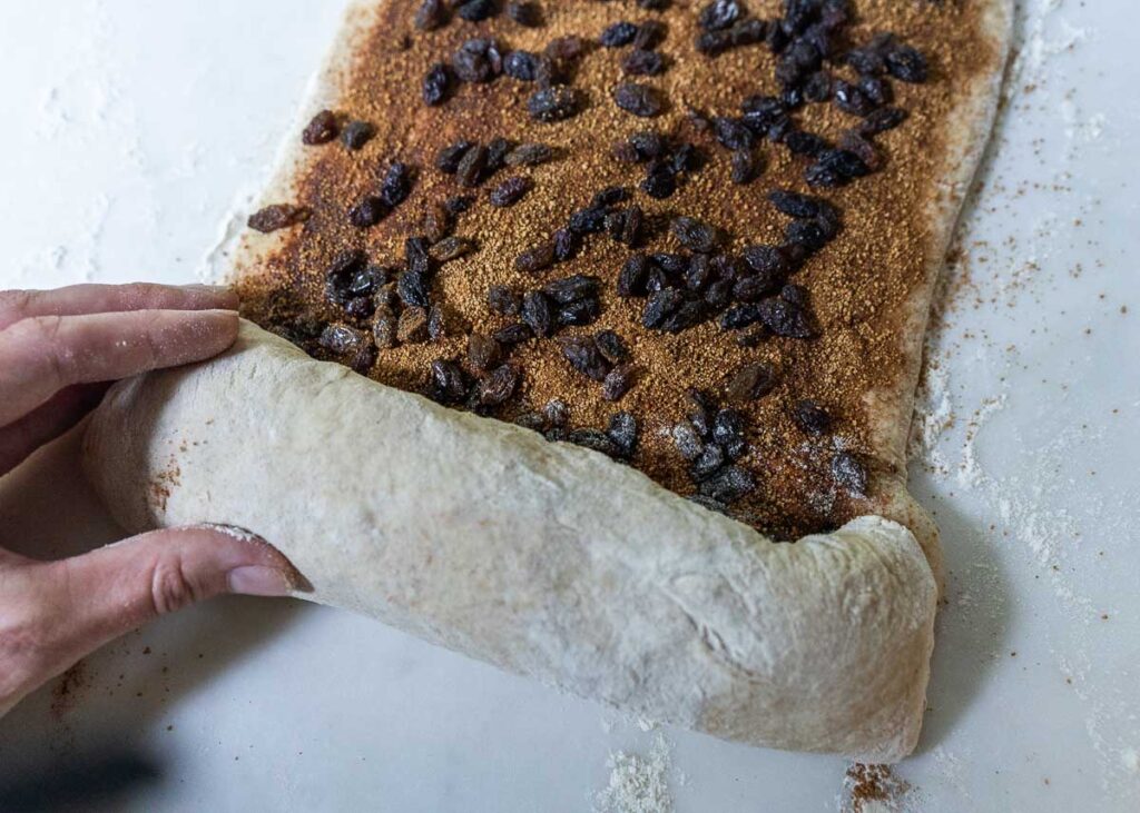 hands rolling up sourdough cinnamon swirl bread