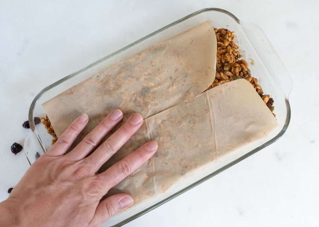 pressing homemade granola bars into a baking dish